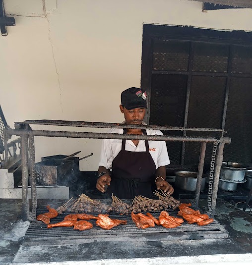 Cook tending mshikaki skewers and grilled chicken over a charcoal grill