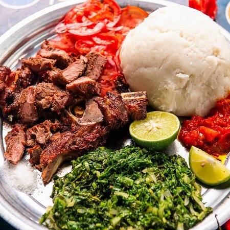 Ugali served with grilled meat, greens, tomato, and lime